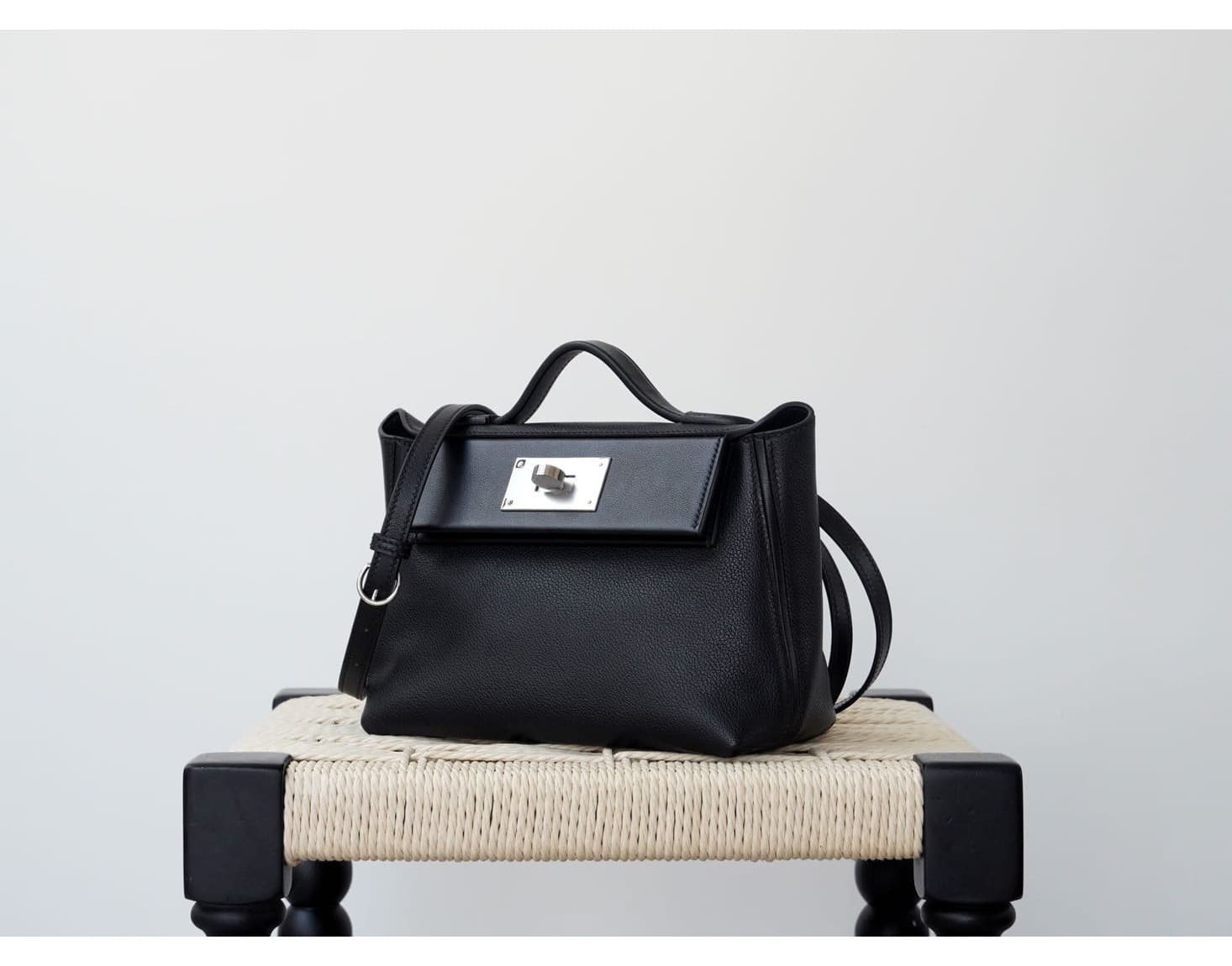 Front view of an Etoupe grey pebbled leather mini doctor bag with white contrast stitching and silver hardware, placed on a white woven stool - 2
