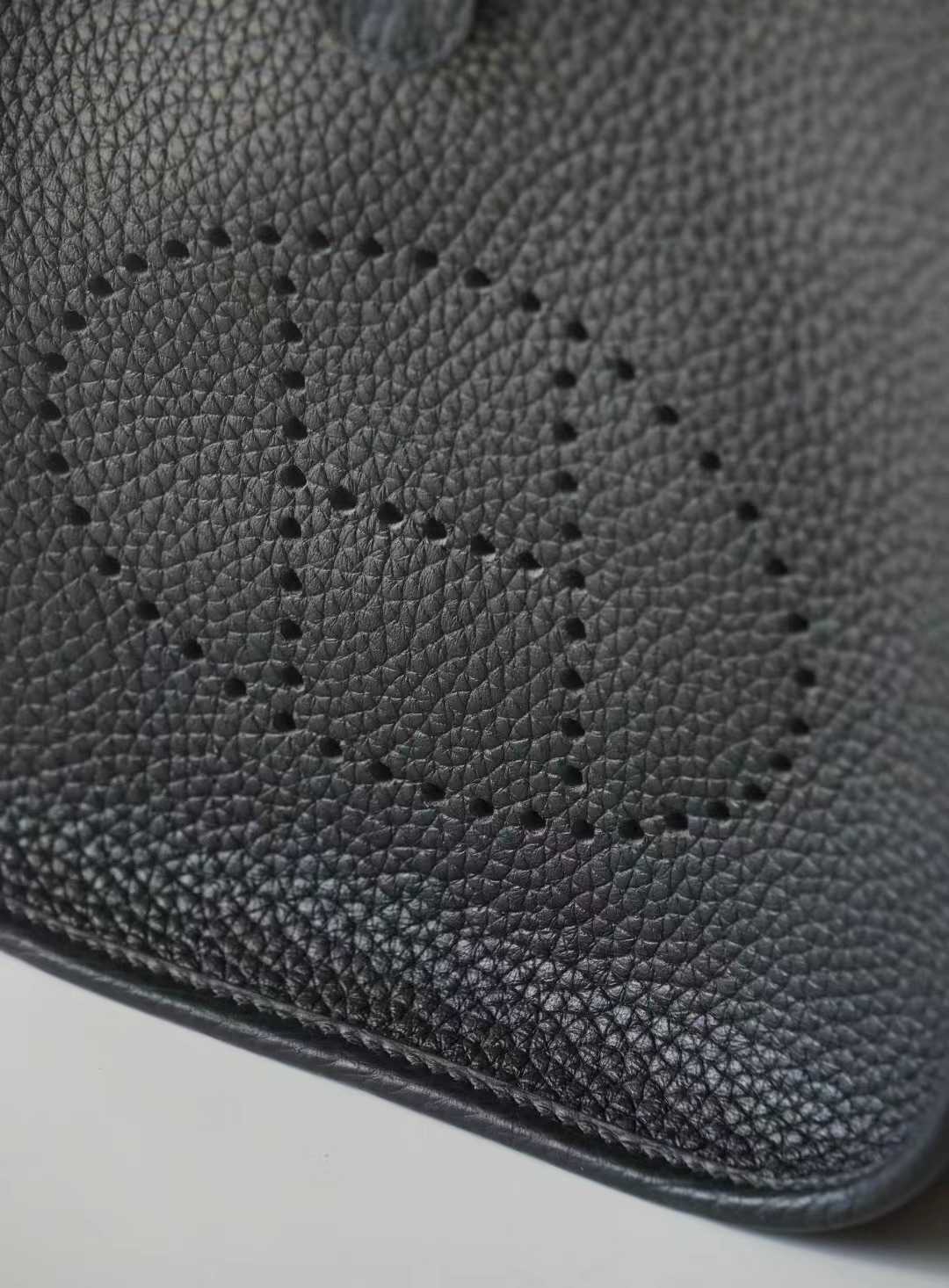 Linjin Luxury togo cowhide crossbody bag with perforated H-motif front panel, snap tab closure, and adjustable canvas strap with silver-tone hardware, on a woven rattan bench - 6
