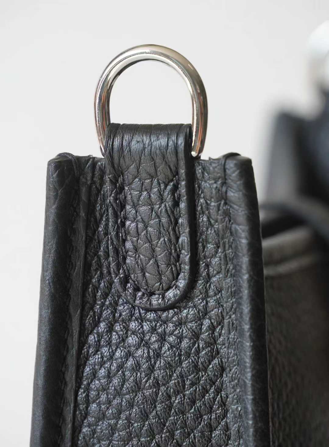 Linjin Luxury togo cowhide crossbody bag with perforated H-motif front panel, snap tab closure, and adjustable canvas strap with silver-tone hardware, on a woven rattan bench - 7