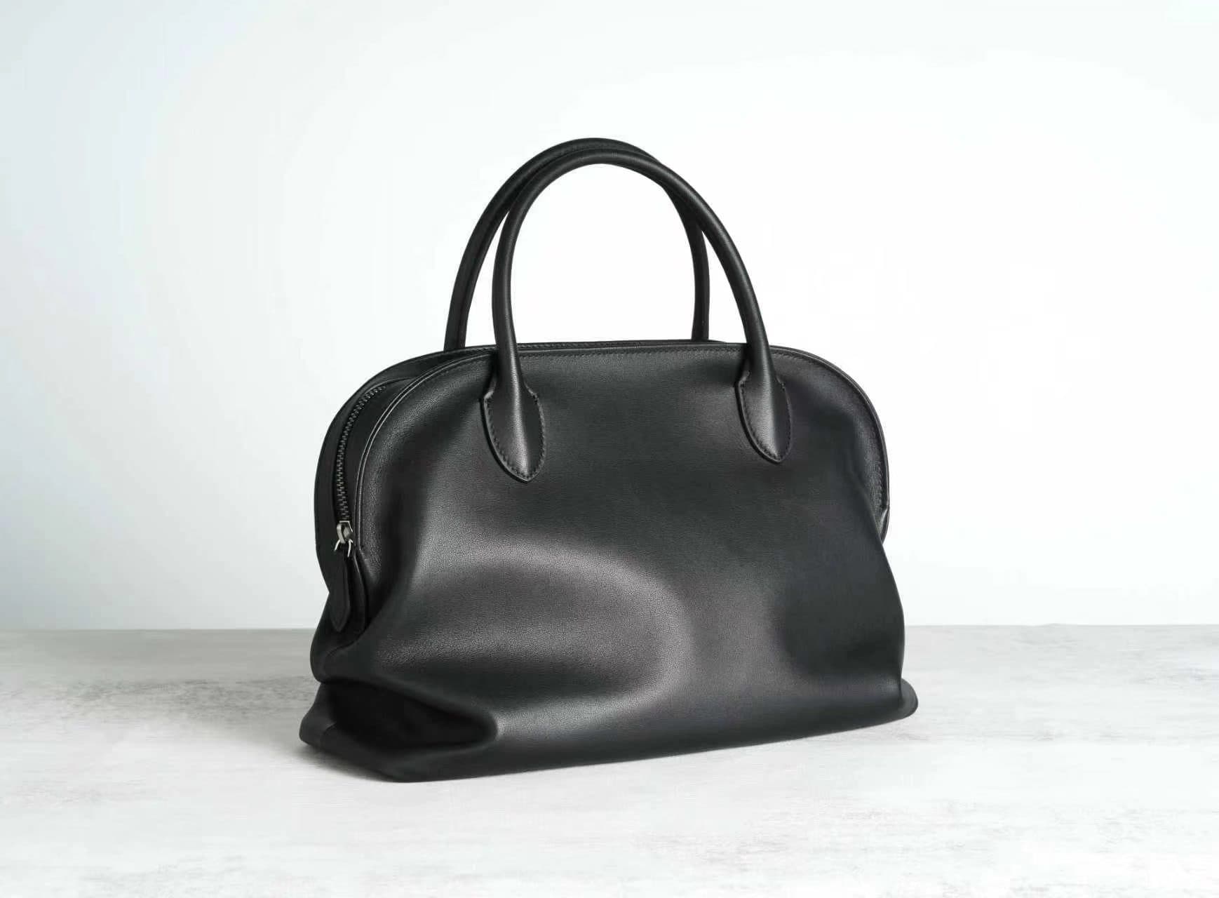 Linjin Luxury polished saddle leather dome bowling bag with natural drape and soft fold texture, dual rolled top handles, structured silhouette, on a light grey surface - 2