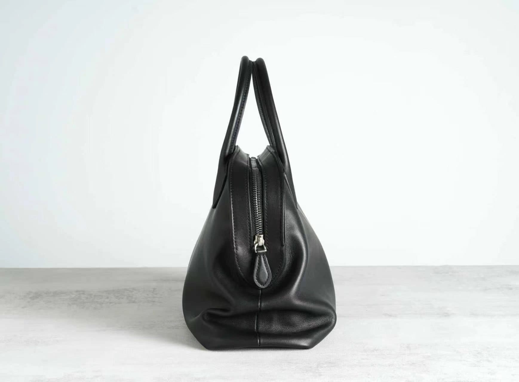 Linjin Luxury polished saddle leather dome bowling bag with natural drape and soft fold texture, dual rolled top handles, structured silhouette, on a light grey surface - 3