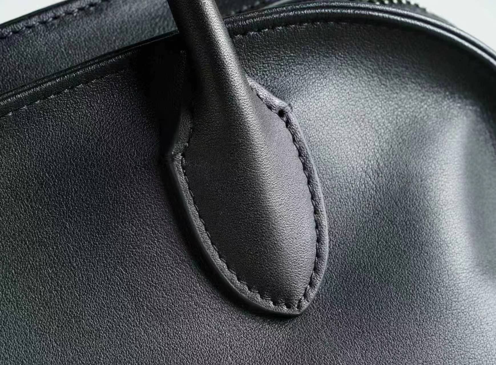 Linjin Luxury polished saddle leather dome bowling bag with natural drape and soft fold texture, dual rolled top handles, structured silhouette, on a light grey surface - 8