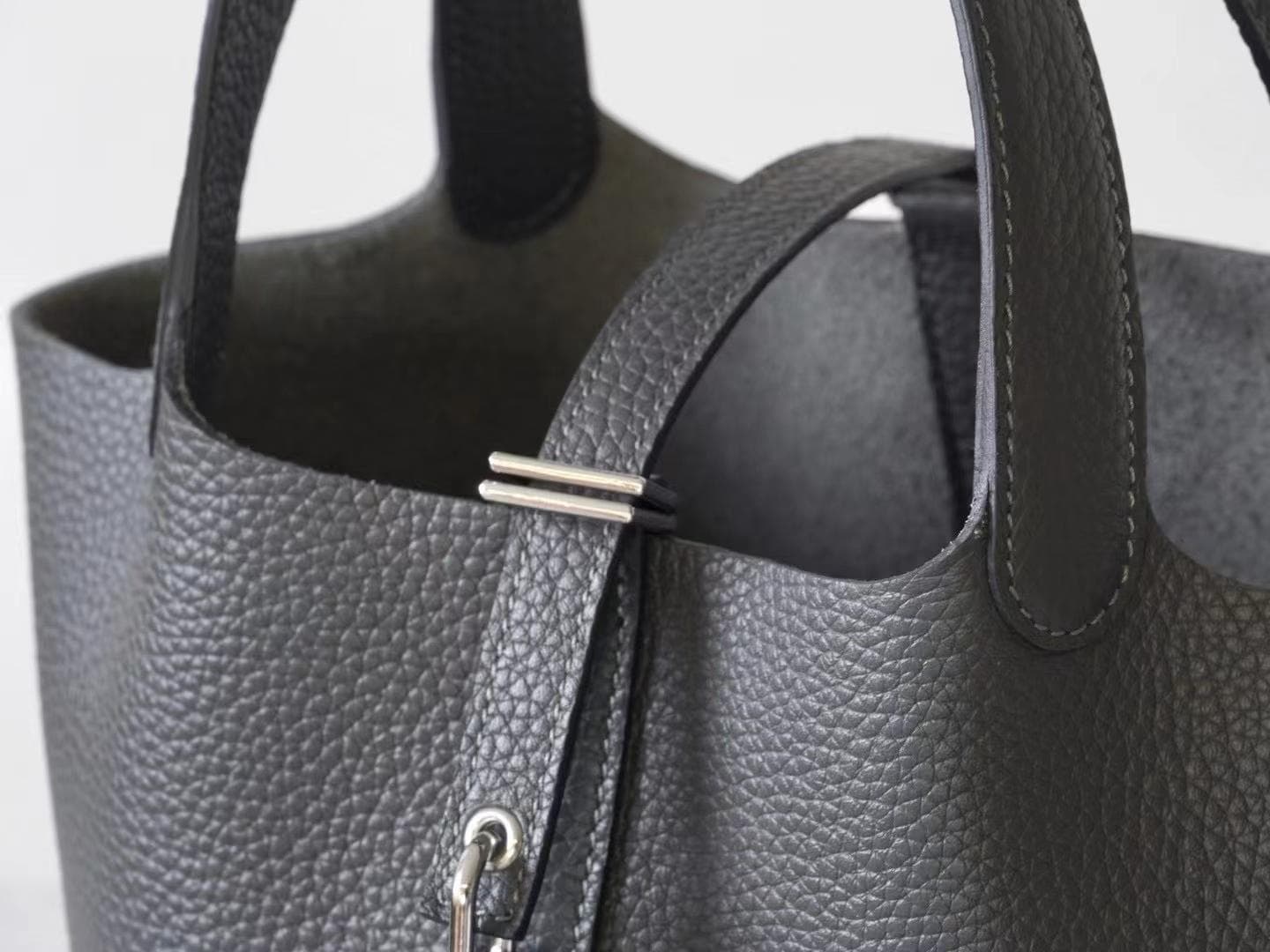 Linjin Luxury black pebbled leather bucket bag with dual top handles, center strap buckle closure, and silver padlock with key charm pendant, displayed on a woven rattan stool - 3