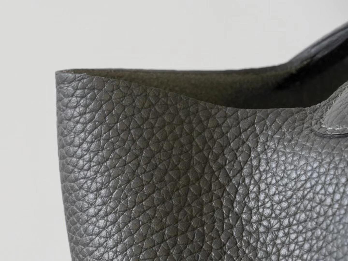 Linjin Luxury black pebbled leather bucket bag with dual top handles, center strap buckle closure, and silver padlock with key charm pendant, displayed on a woven rattan stool - 4