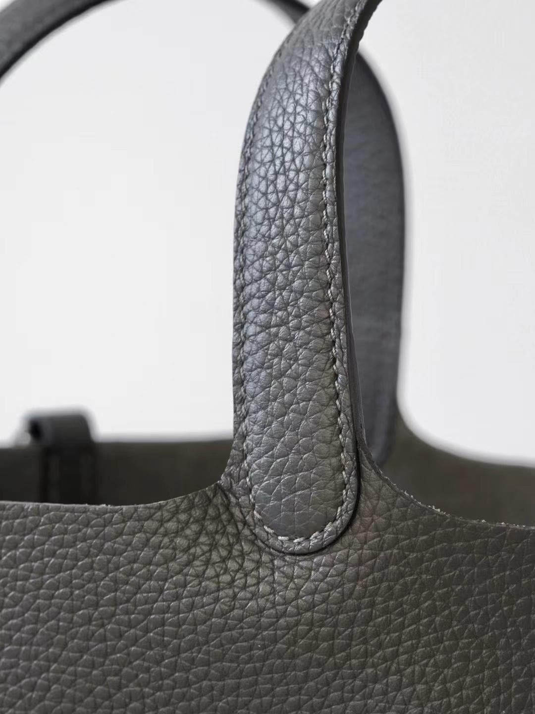 Linjin Luxury black pebbled leather bucket bag with dual top handles, center strap buckle closure, and silver padlock with key charm pendant, displayed on a woven rattan stool - 6