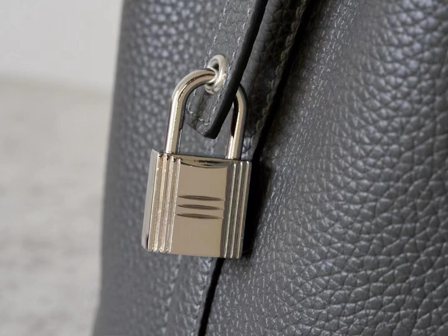 Linjin Luxury black pebbled leather bucket bag with dual top handles, center strap buckle closure, and silver padlock with key charm pendant, displayed on a woven rattan stool - 9