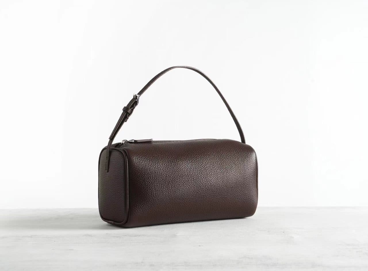 Linjin Luxury leather cylinder bags in six colors — black, burgundy, beige, red, off-white, and dark brown — displayed on a woven rattan bench with black bobbin legs - 2