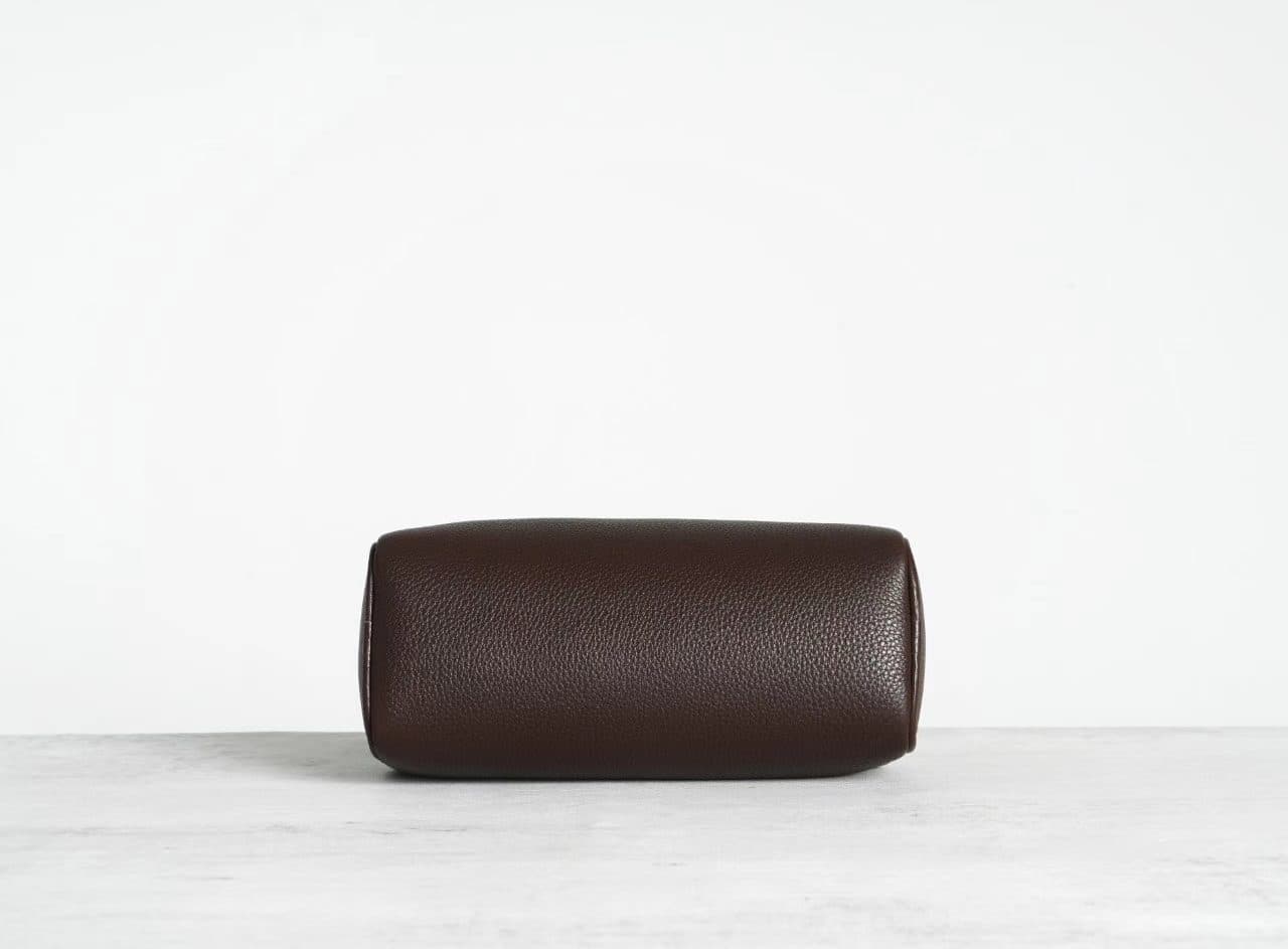 Linjin Luxury leather cylinder bags in six colors — black, burgundy, beige, red, off-white, and dark brown — displayed on a woven rattan bench with black bobbin legs - 3