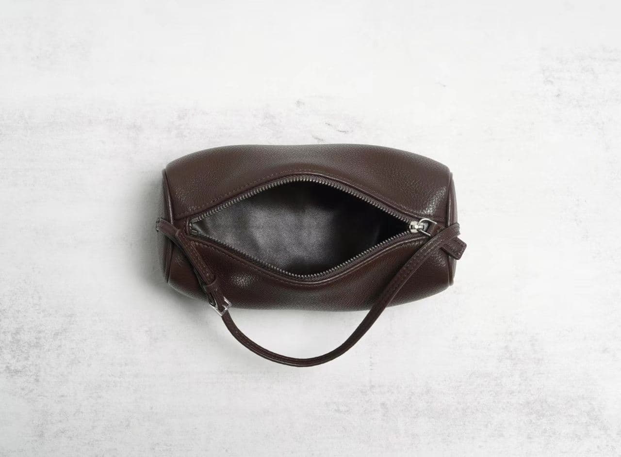 Linjin Luxury leather cylinder bags in six colors — black, burgundy, beige, red, off-white, and dark brown — displayed on a woven rattan bench with black bobbin legs - 6