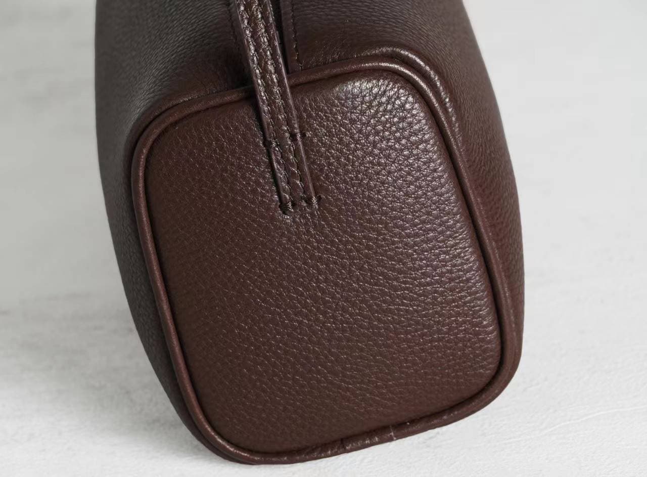 Linjin Luxury leather cylinder bags in six colors — black, burgundy, beige, red, off-white, and dark brown — displayed on a woven rattan bench with black bobbin legs - 8