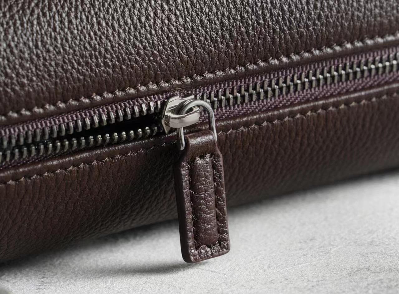 Linjin Luxury leather cylinder bags in six colors — black, burgundy, beige, red, off-white, and dark brown — displayed on a woven rattan bench with black bobbin legs - 9