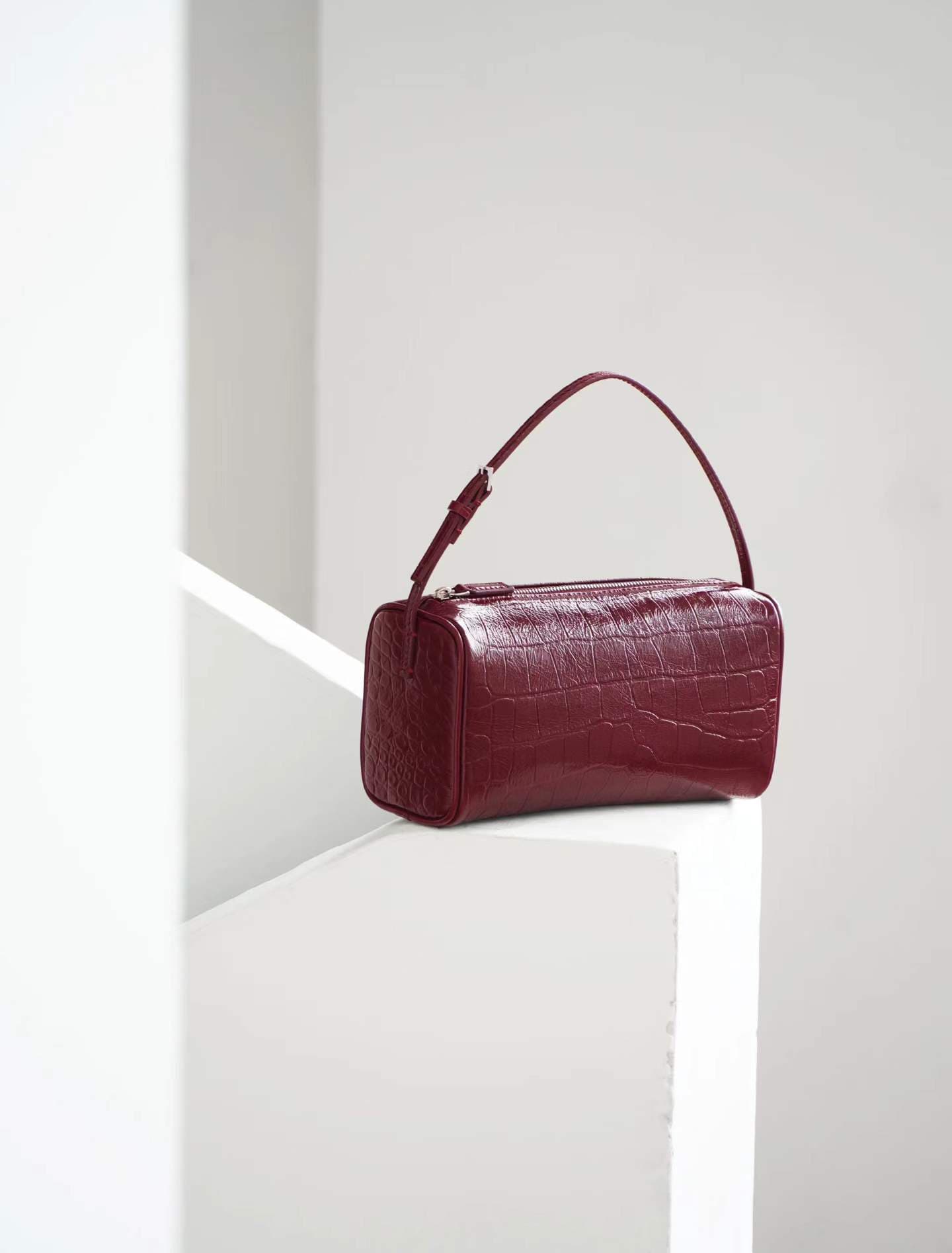 Linjin Luxury croc-embossed lambskin cylinder bags in black, cream, and burgundy, stacked on a woven rattan bench with black bobbin legs, silver zip hardware and adjustable shoulder straps - 5