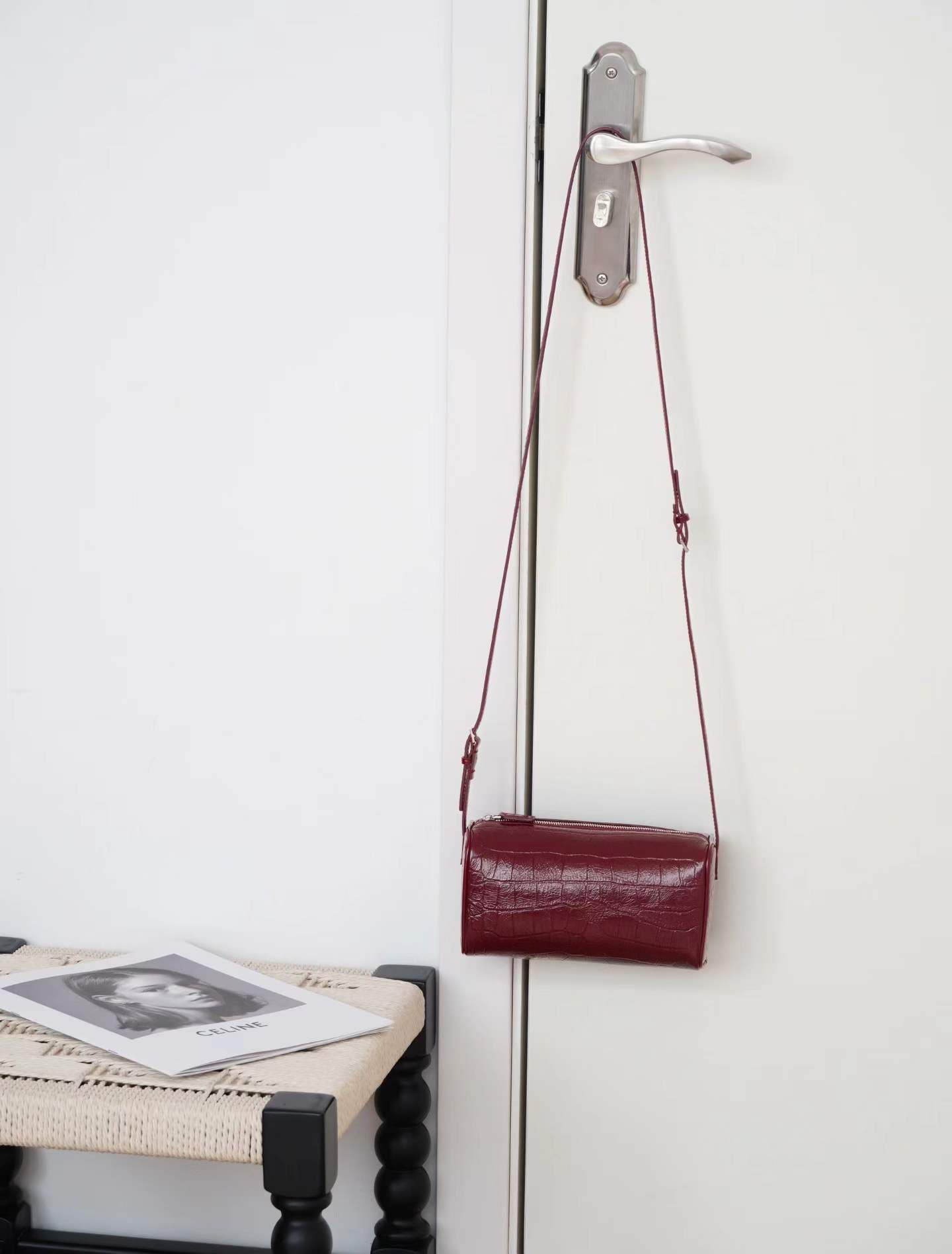 Linjin Luxury croc-embossed lambskin cylinder bags in black, cream, and burgundy, stacked on a woven rattan bench with black bobbin legs, silver zip hardware and adjustable shoulder straps - 6