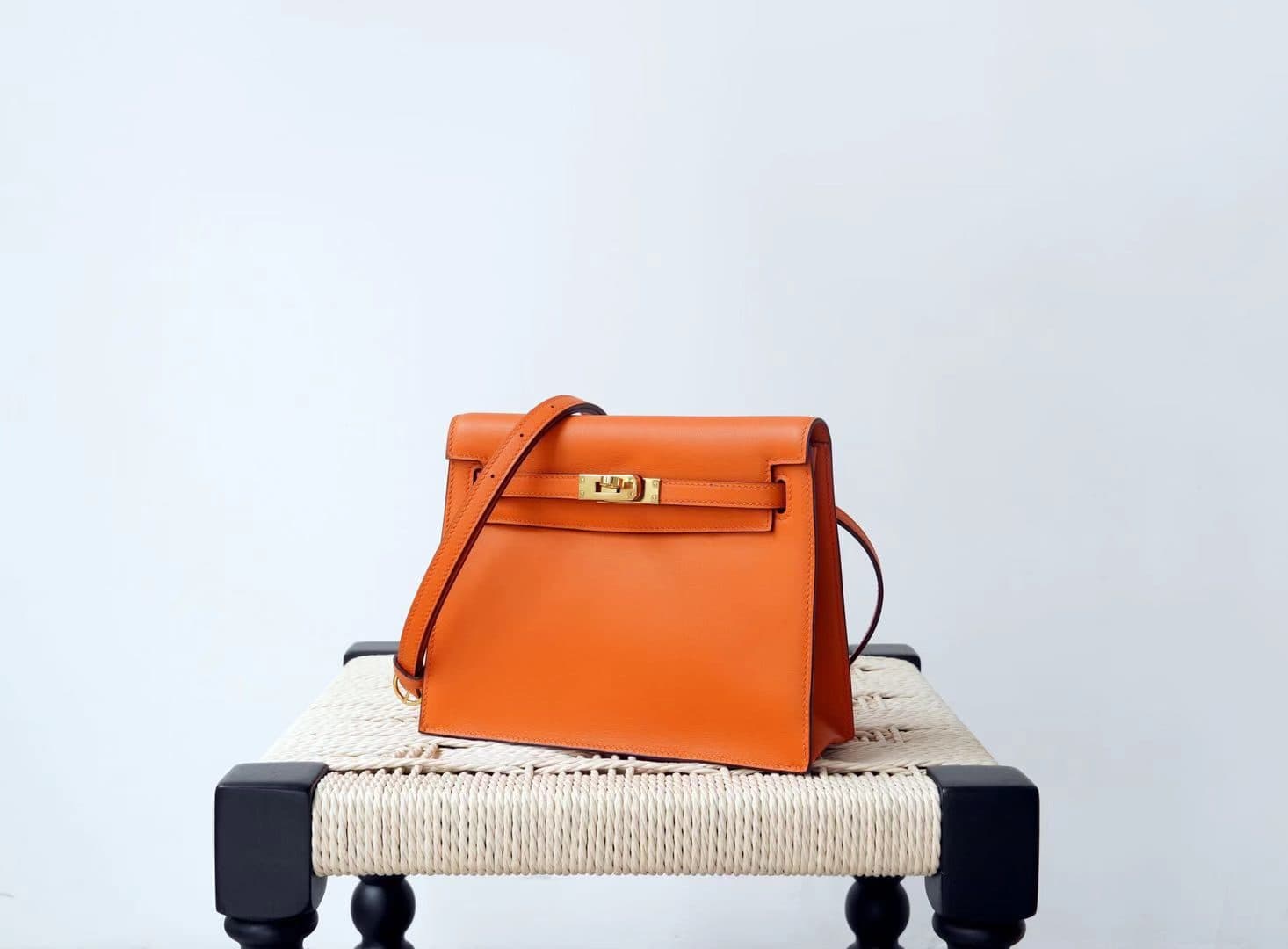 Linjin Luxury black evercolor leather dance bag with silver turn-lock closure, adjustable crossbody strap, hand-painted burnished edges, displayed on a woven rattan bench with black bobbin legs - 2
