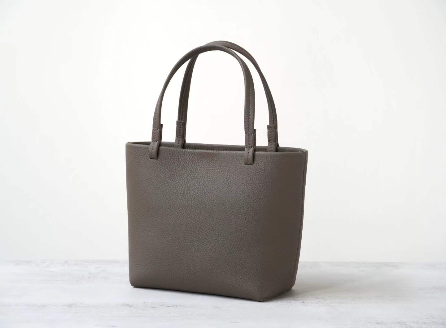 Linjin Luxury taupe pebbled cowhide oversized knotted tote bag with slim leather handles tied at top, minimal hardware-free design, on a white background - 2